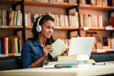Eine Jugendliche sitzt in der Bücherei vor einem PC und hält ein Buch