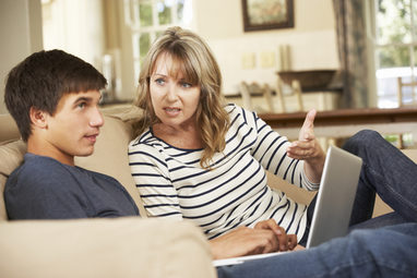 Sohn sitzt mit Laptop neben seiner Mutter auf dem Sofa