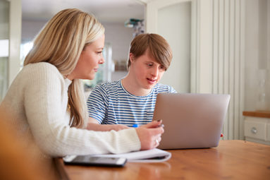 Frau und Jugendlicher sitzen am Tisch vor einem aufgeklappten Laptop