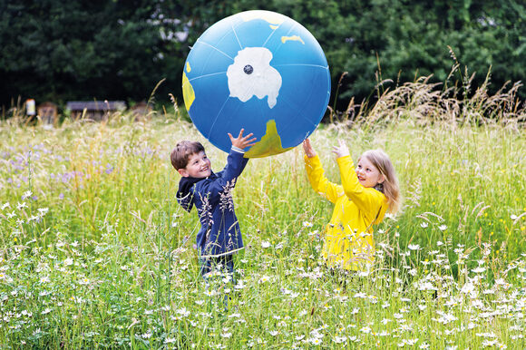 Kinder werfen Erdball auf Wiese