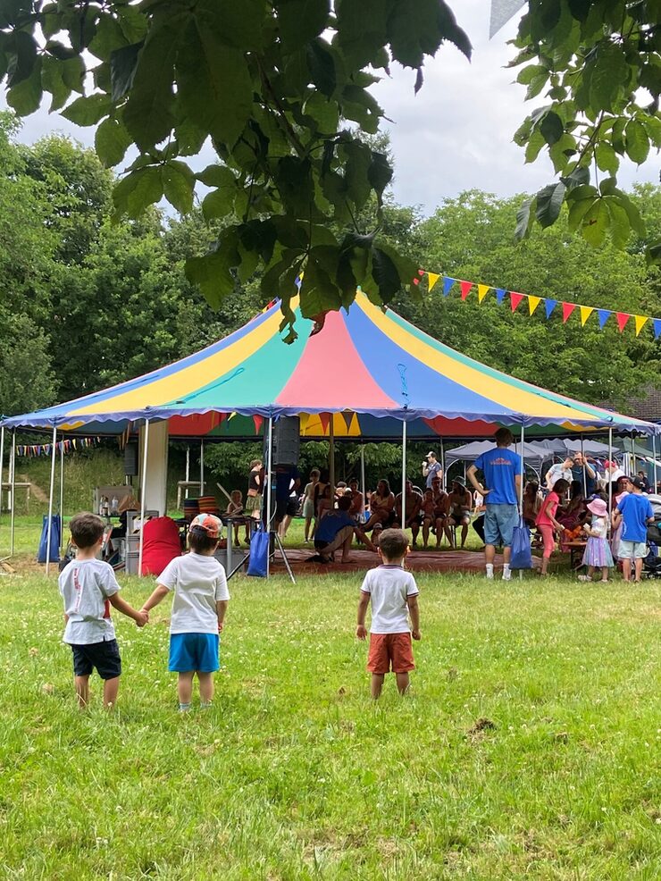 Kleine Kinder vor einem bunten offenen Festzelt mit weiteren Personen