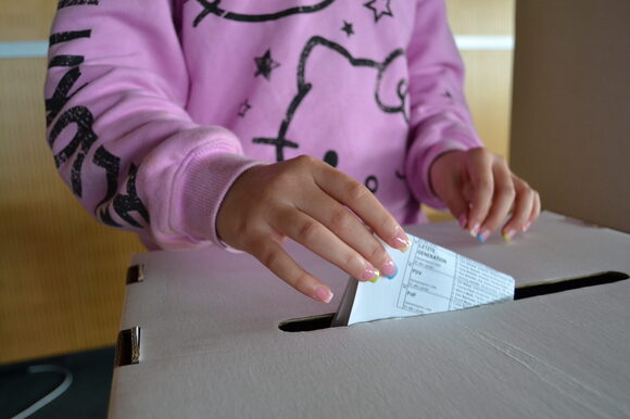 Ein Kind wirft einen Stimmzettel in eine Wahlurne