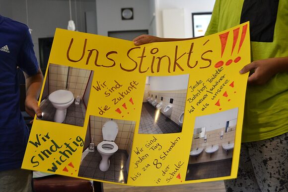 Kinder mit Plakat "Uns Stinkts...." zum Toilettenproblem