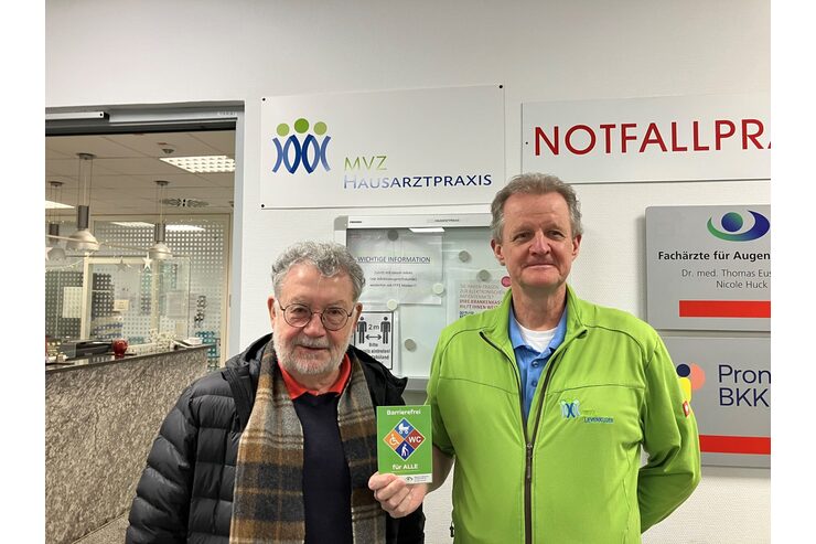 Zwei Personen stehen in der Praxis und halten das Barrierefrei-Siegel